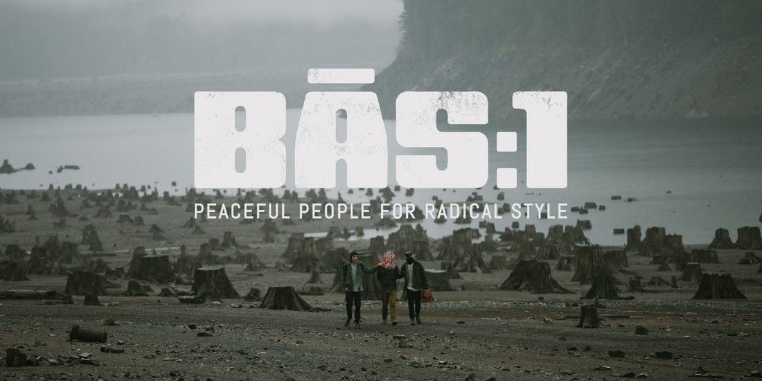 Three friends walk arm-in-arm across a misty, tree-stump-strewn shoreline, embodying BAS:1’s radical style with peaceful intent.