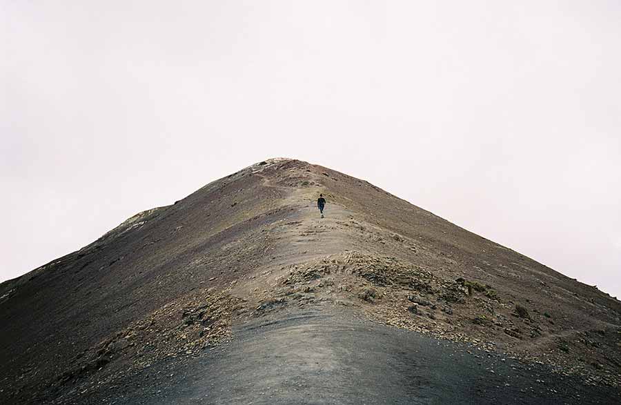 Solo hiker ascends rugged mountain peak under soft overcast sky, embodying adventure and solitude.