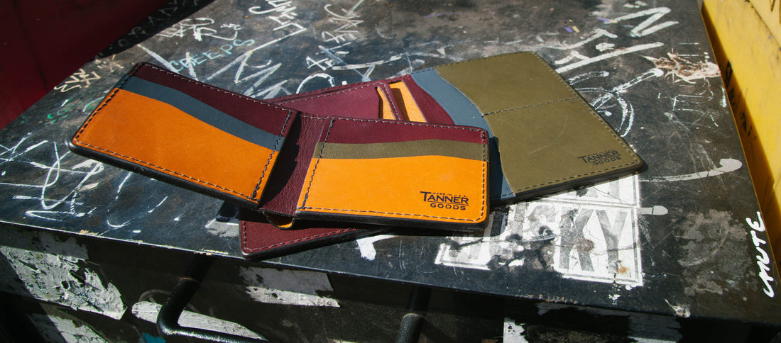 Colorful Tanner Goods wallets stacked on a graffiti-covered urban surface, blending craftsmanship with street edge.