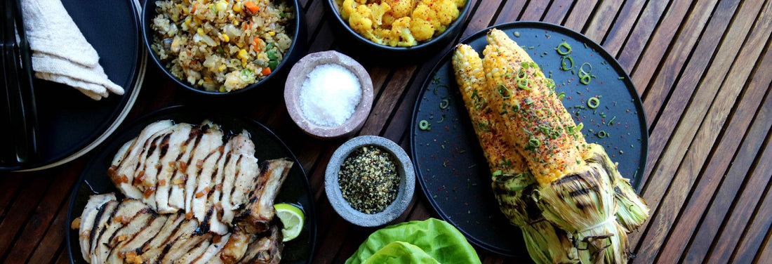 Grilled chicken, corn, and colorful sides on a rustic wooden table, evoking warmth and shared meals.