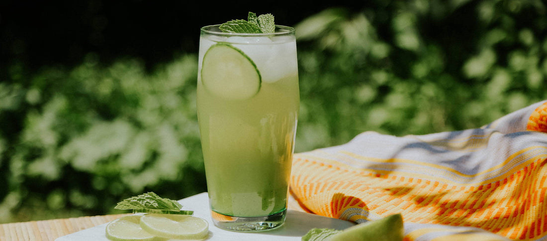Refreshing cucumber mint drink with lime slices, set on a sunny patio with greenery and a colorful towel.