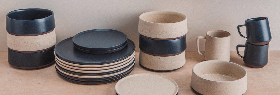 Stacked ceramic bowls, plates, and mugs in earthy tones on a wooden surface, showcasing minimalist design and craftsmanship.