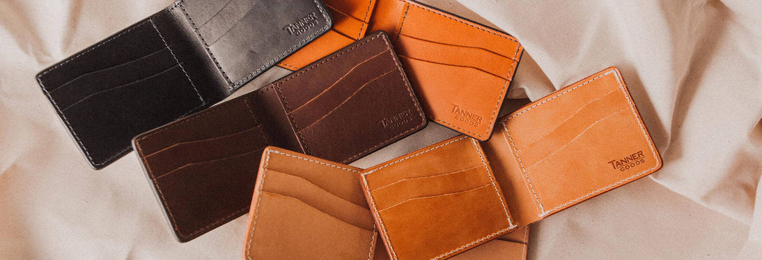 Four Tanner Goods leather wallets in black, brown, and tan, neatly arranged on soft fabric, showcasing premium craftsmanship and timeless design.