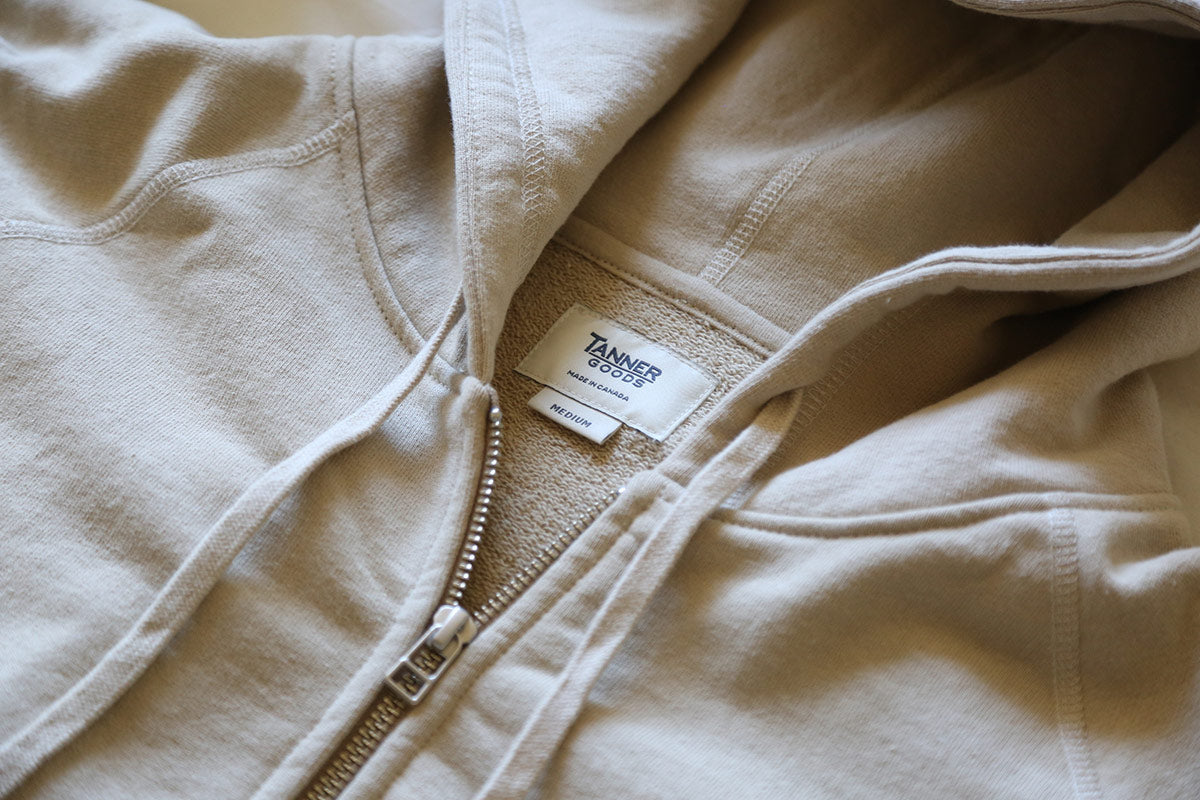 Soft beige zip hoodie with Tanner Goods label, rustic neutral tones, cozy woodland essentials.