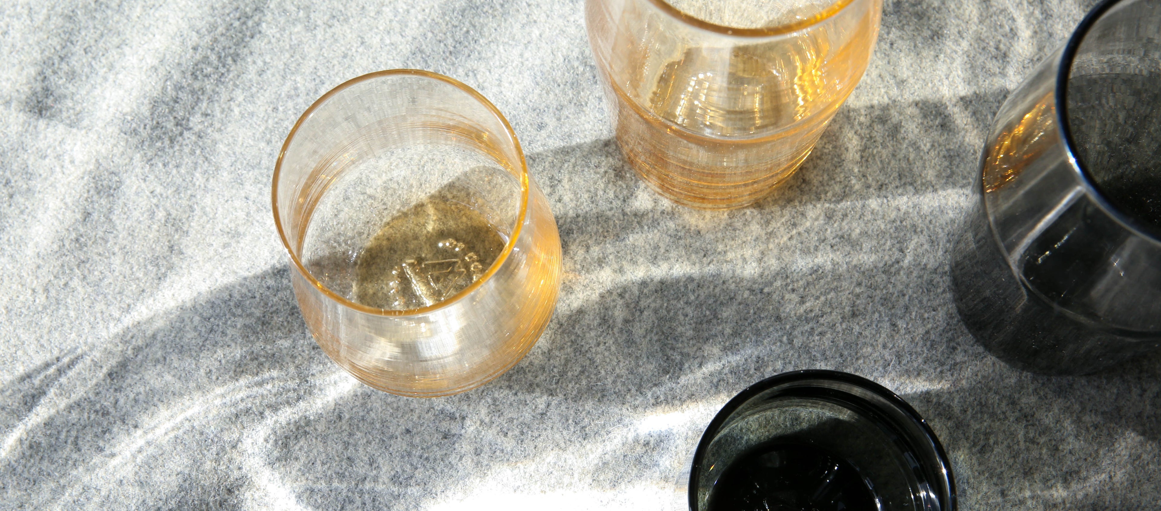 Amber and black textured tumblers on soft gray felt, glowing in sunlight — elegant, modern drinkware for festive gatherings.