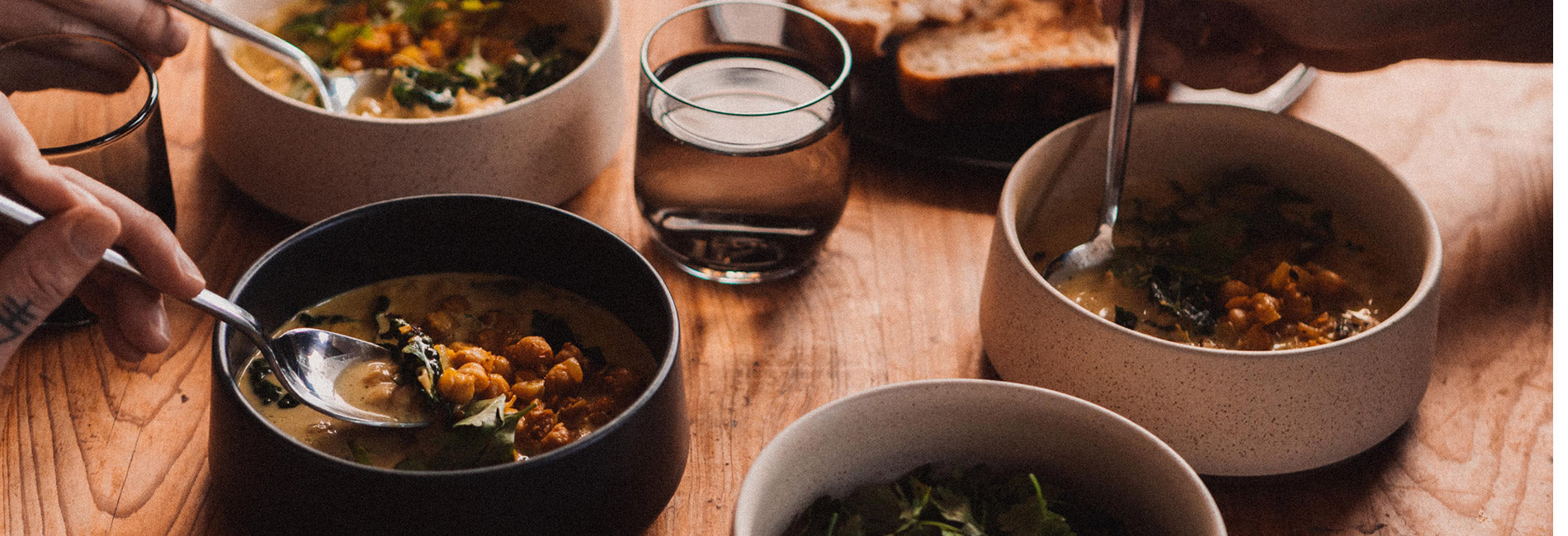 Warm, rustic ceramic bowls filled with hearty soup, shared on a wooden table with bread and water—cozy, communal holiday dining.