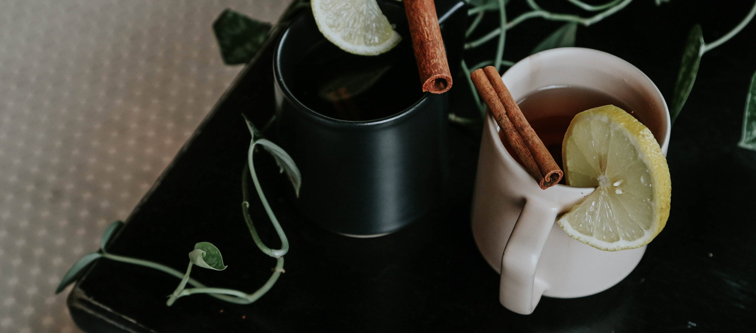 Minimalist ceramic mugs in black and cream with lemon and cinnamon, styled for cozy, natural wellness moments.