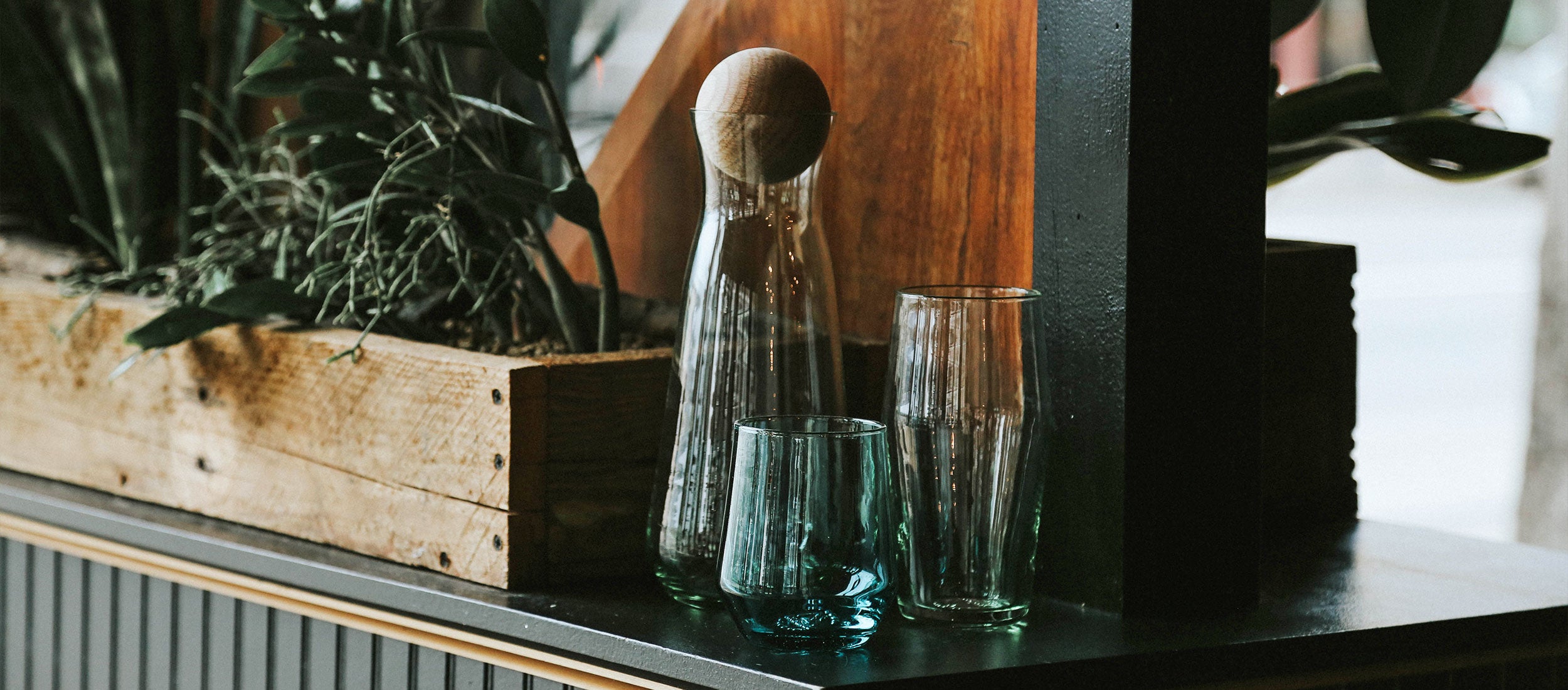 Elegant ribbed glassware in deep teal and amber, paired with wooden accents and greenery, evoking warm, natural sophistication.