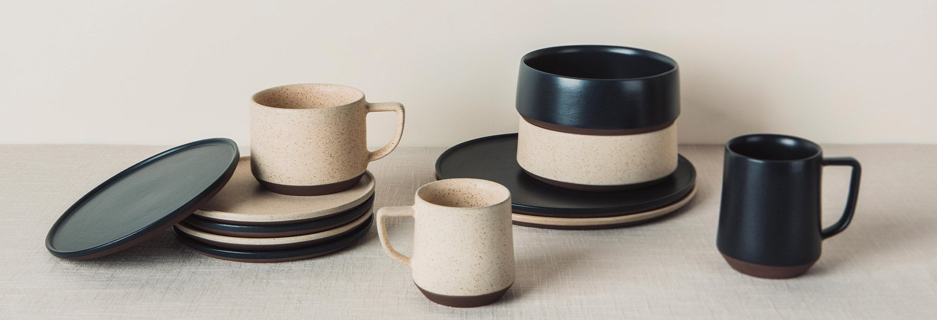 Earthy ceramic dinnerware in speckled beige and matte black, minimalist modern tableware set.