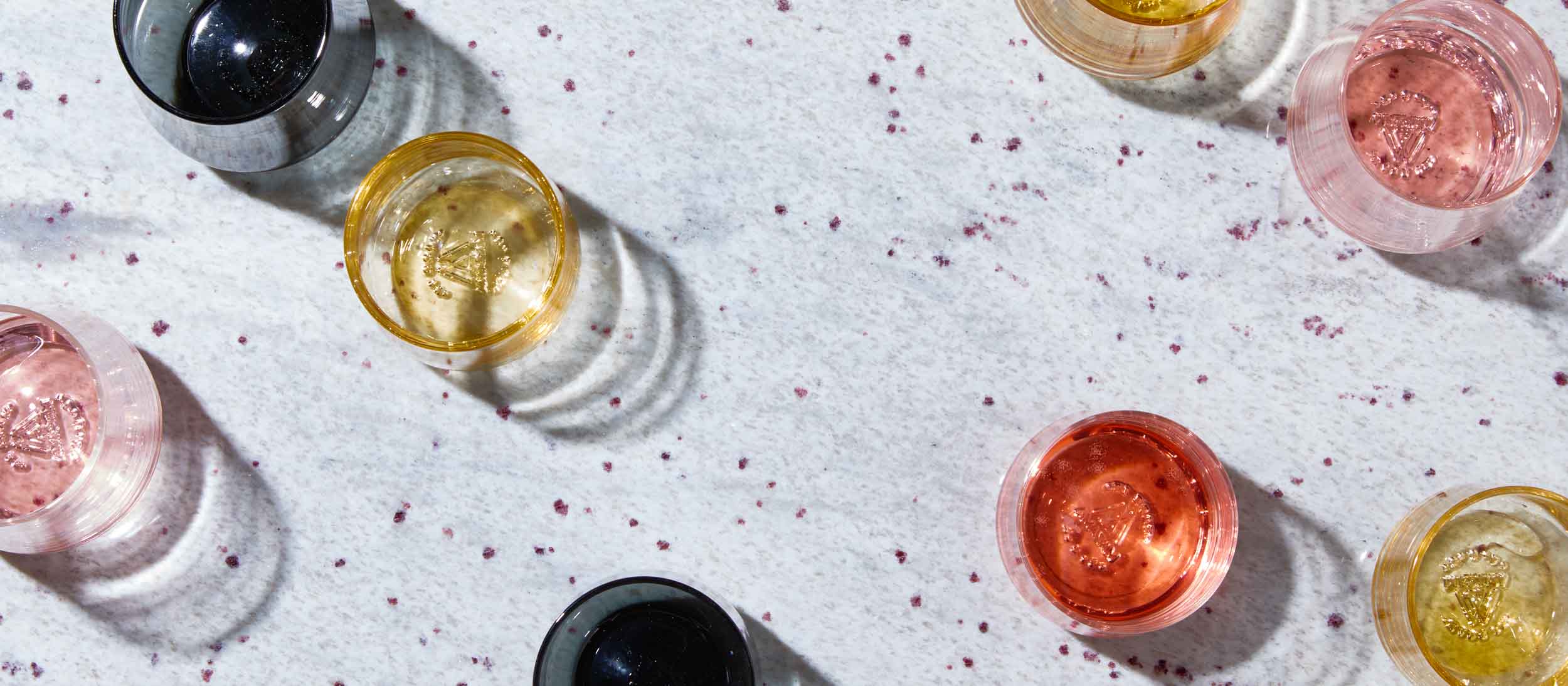Colorful glass tumblers in amber, pink, and black on speckled white surface, evoking modern home entertaining.