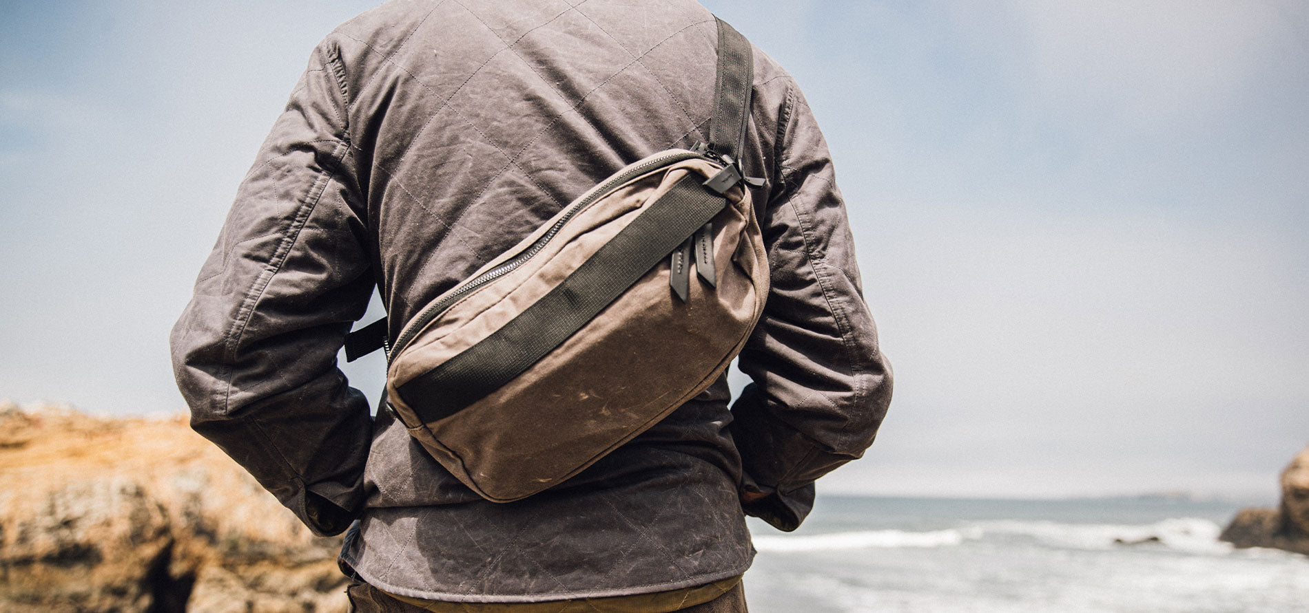 Rugged waxed canvas fanny pack worn by traveler on rocky coast, earthy tones, adventure-ready style.