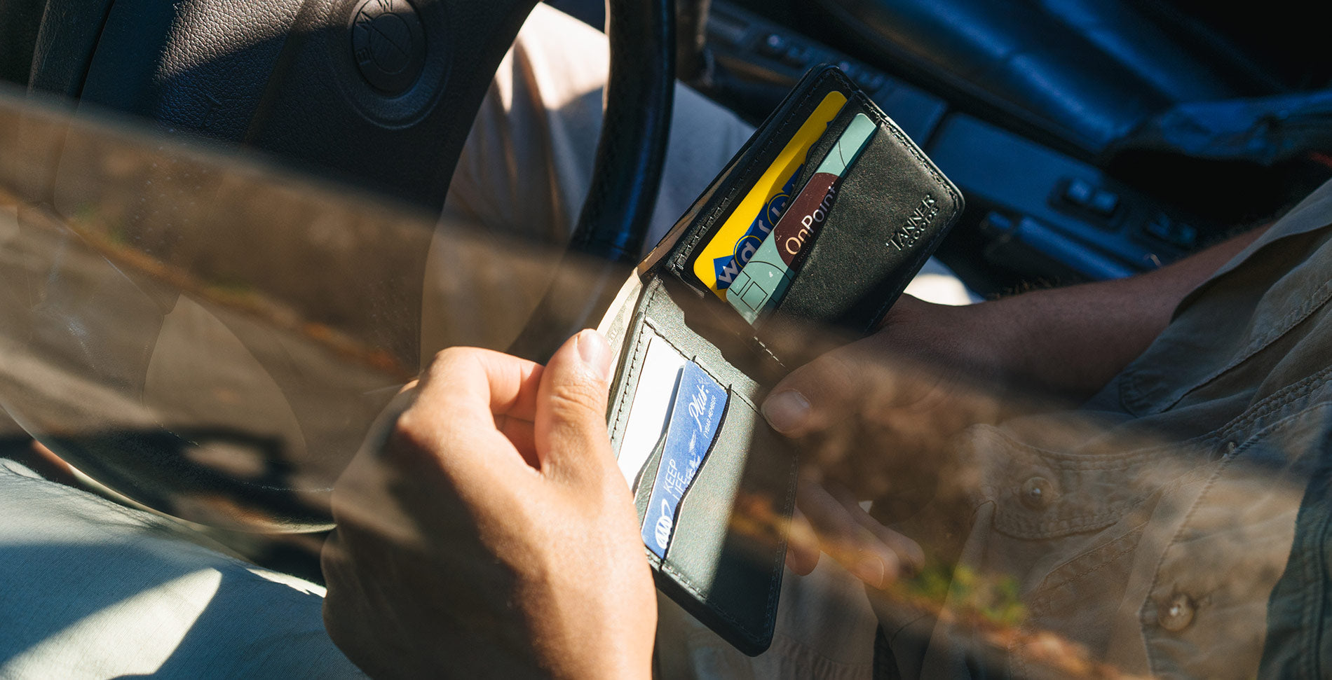 Sleek black leather wallet in hand, inside car, showcasing premium craftsmanship and modern sophistication.