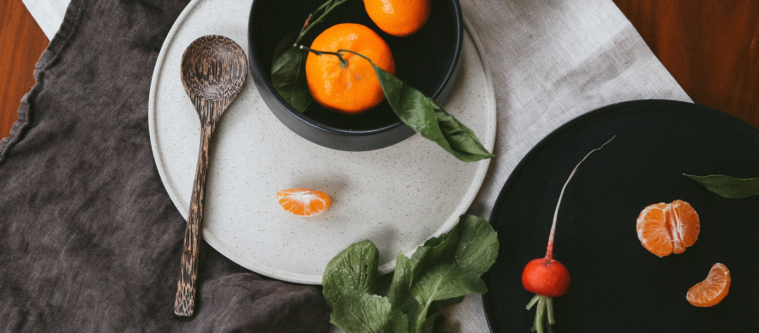 Earthy ceramic plates and bowls in speckled white and matte black, styled with fresh citrus and greens for a minimalist, modern dining aesthetic.