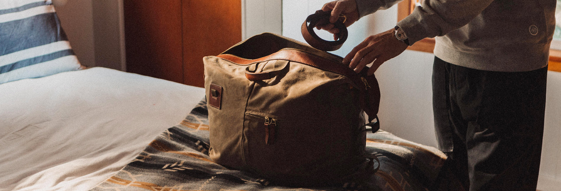 Rugged olive canvas duffel with brown leather accents, packed for adventure in cozy bedroom setting.