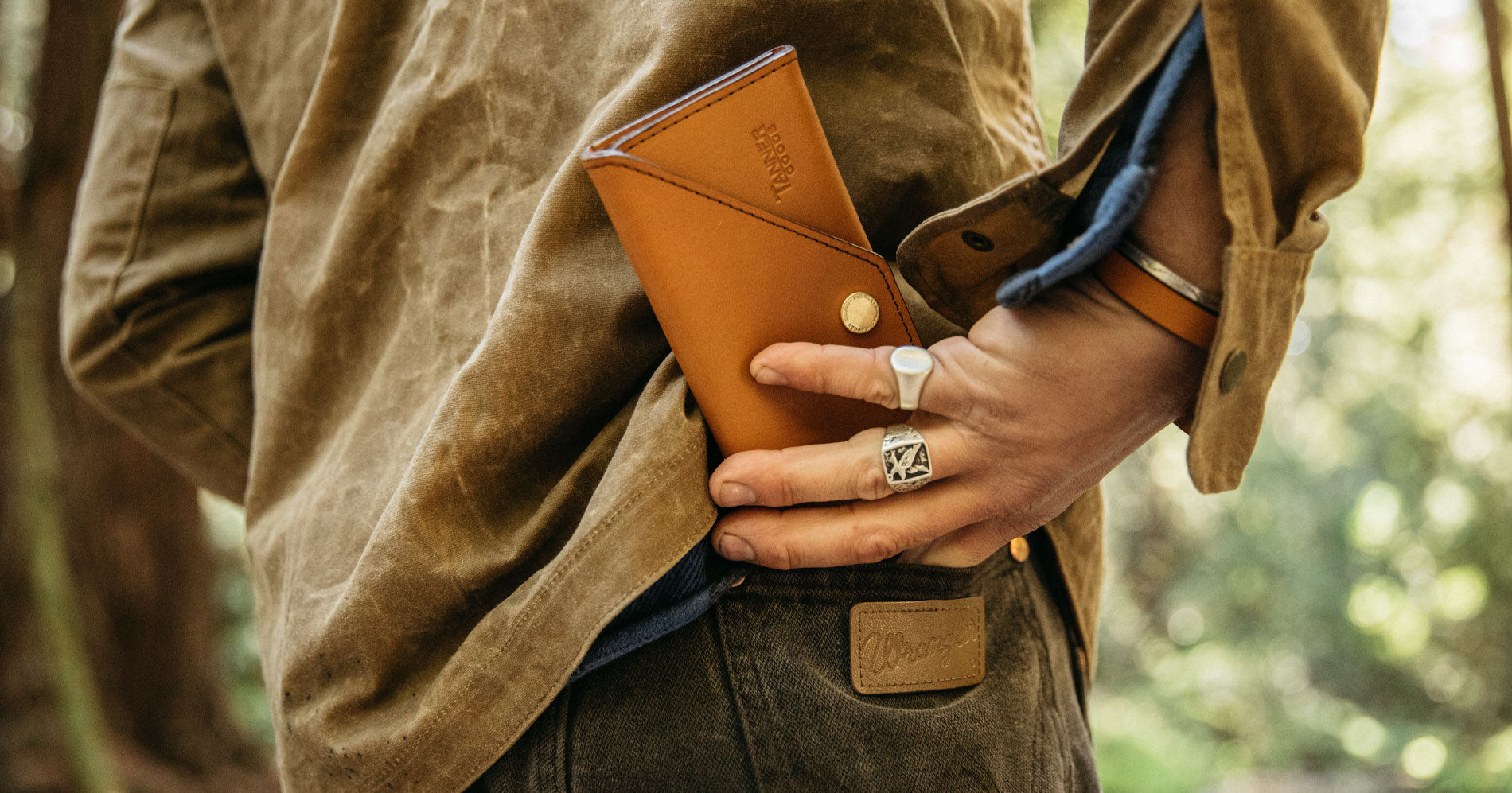 A man's right hand placing a Saddle Tan Workman wallet in the backside of their Wrangler jeans. 
