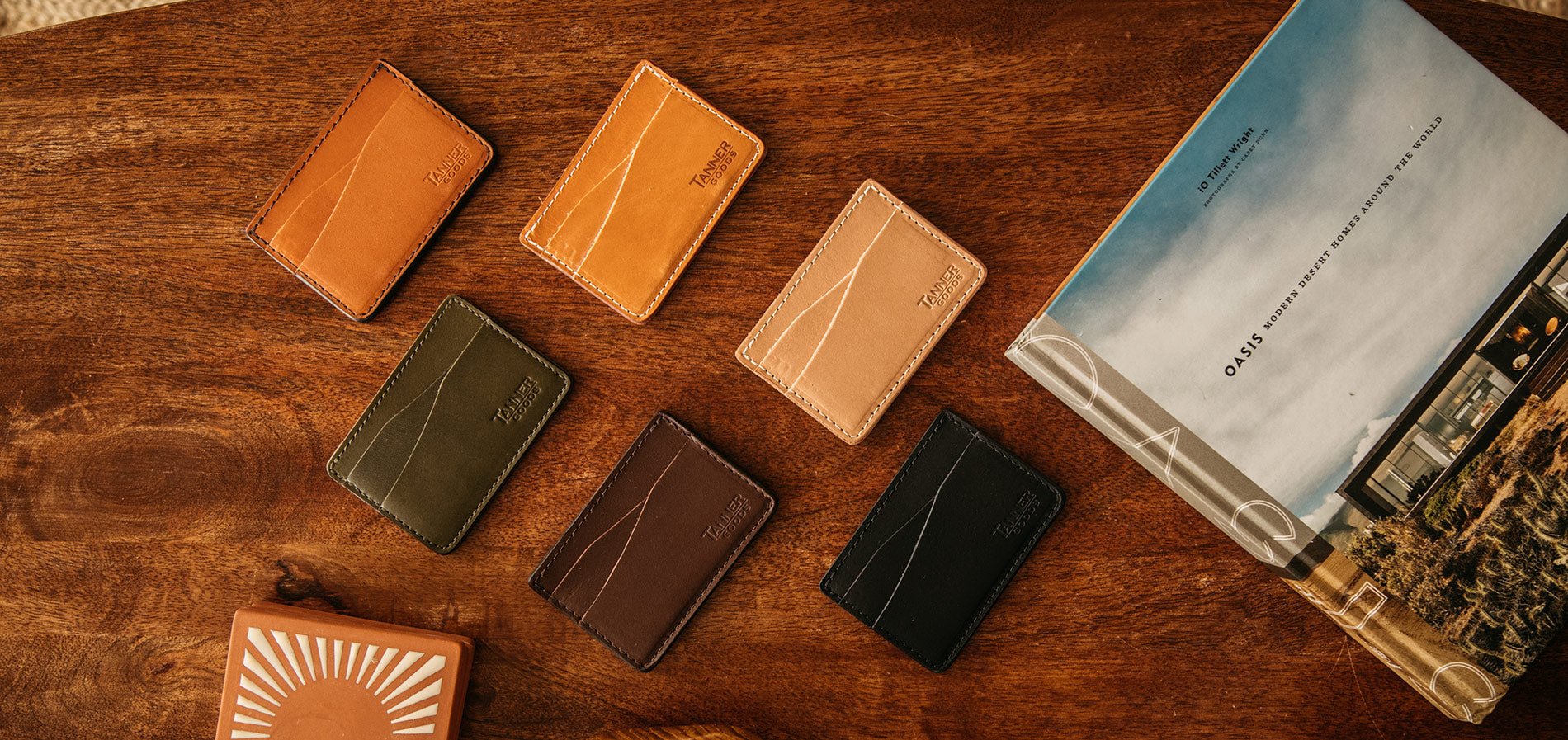 Minimal leather cardholders in earthy tones with contrast stitching, styled on wood with travel-inspired book, evoking adventure and refined craftsmanship.