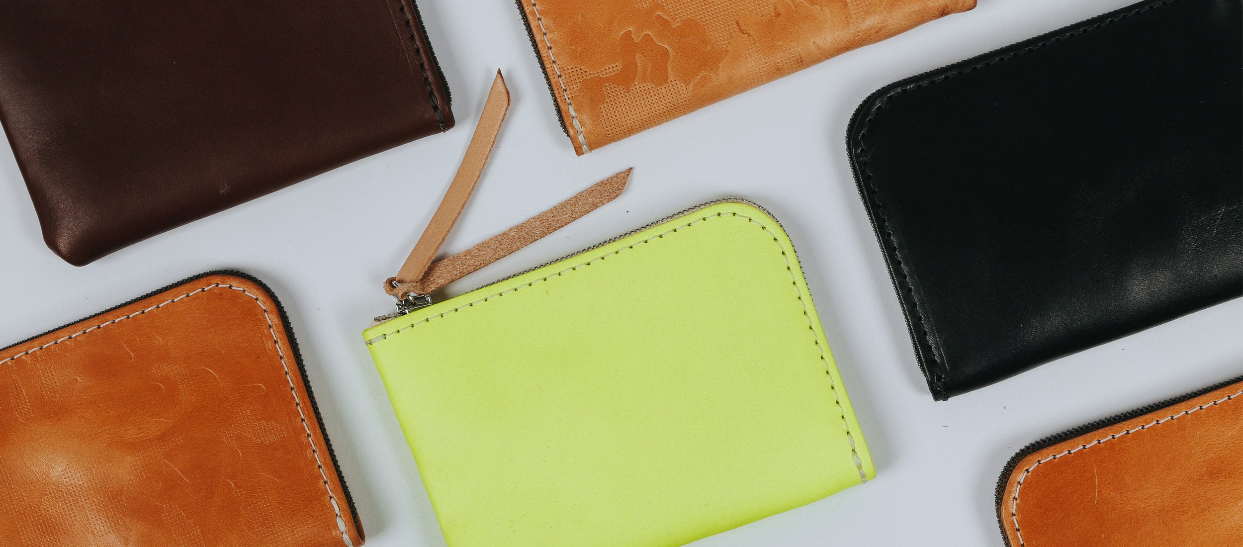 Stylish leather zip wallets in rich brown, tan, black, and vibrant lime green with precise stitching and sleek design.
