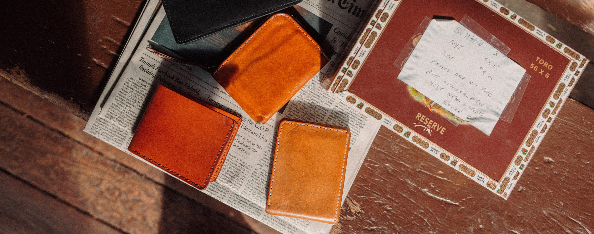 Rich leather card holders in warm amber and black, styled on vintage newspaper and cigar box, evoking timeless craftsmanship and everyday essentials.