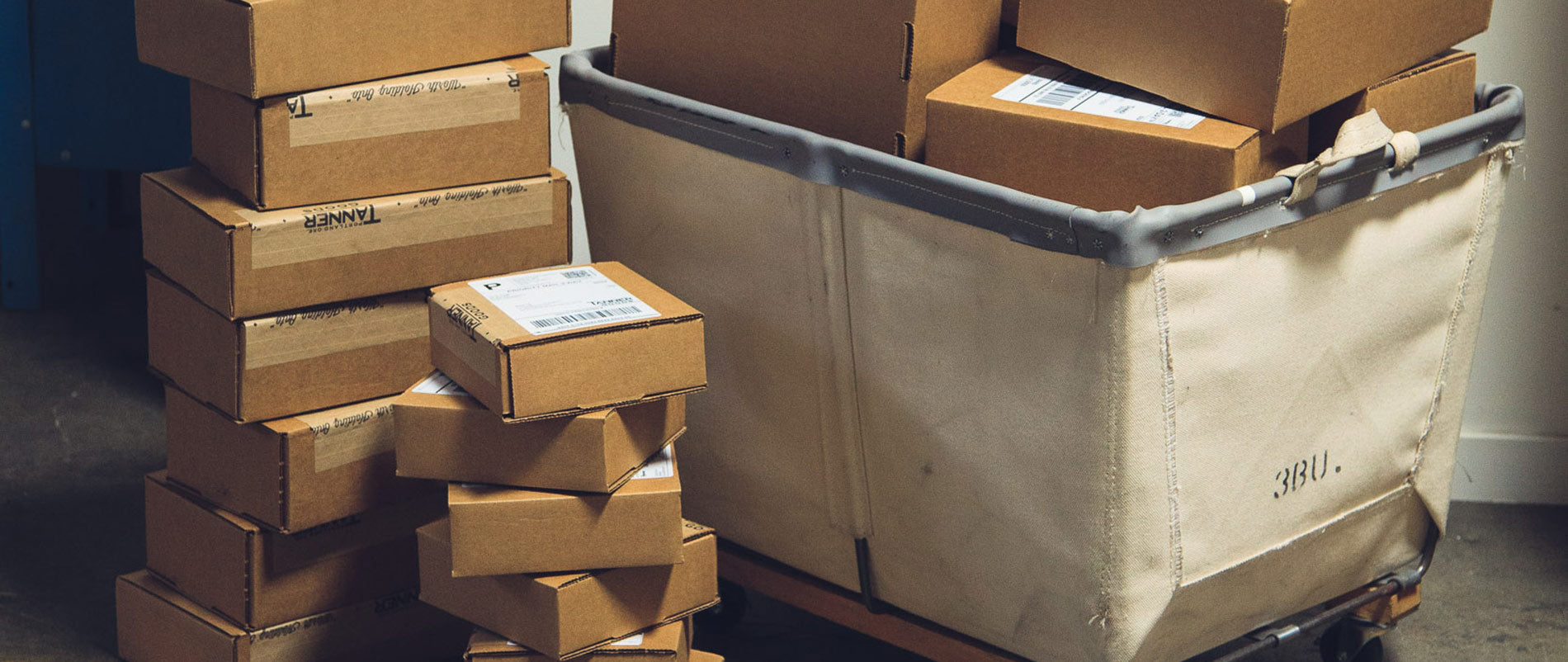 Stacked cardboard boxes and a canvas cart in rustic warehouse setting, exclusive subscriber sale.