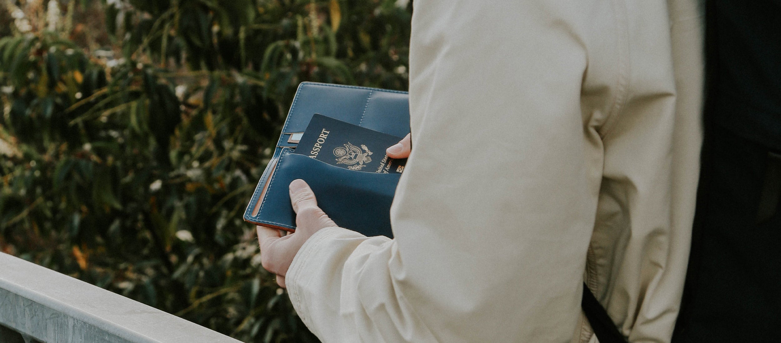 Elegant navy leather passport holder in hand, paired with a beige coat, evoking refined travel style.
