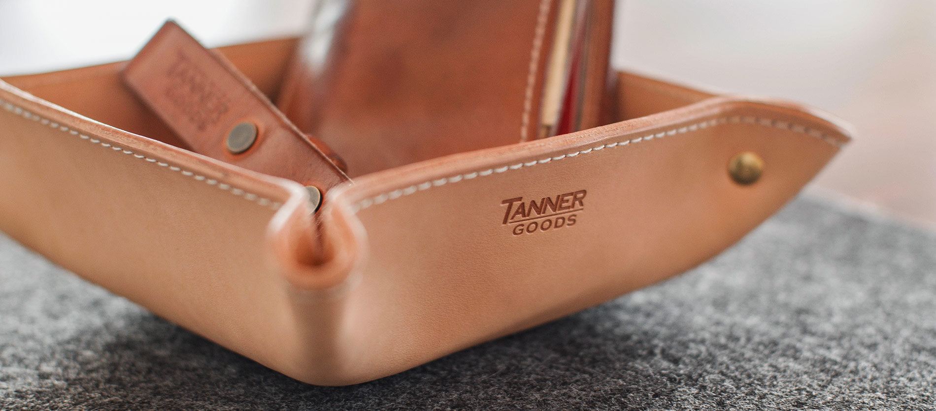 Rich tan leather desk tray with white stitching, holding pens and cards, embodying minimalist home and office elegance.