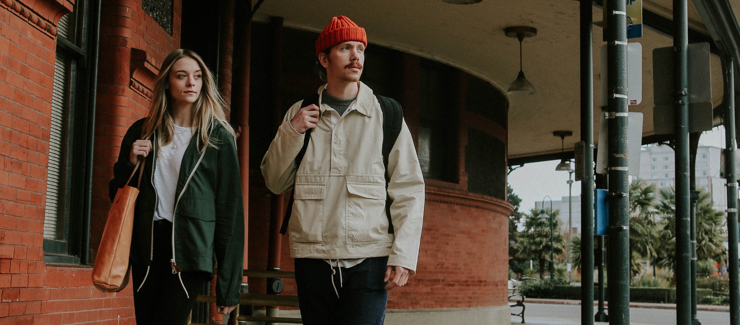 Holiday travel essentials: cozy beige and green jackets, orange beanie, leather tote, urban adventure style.