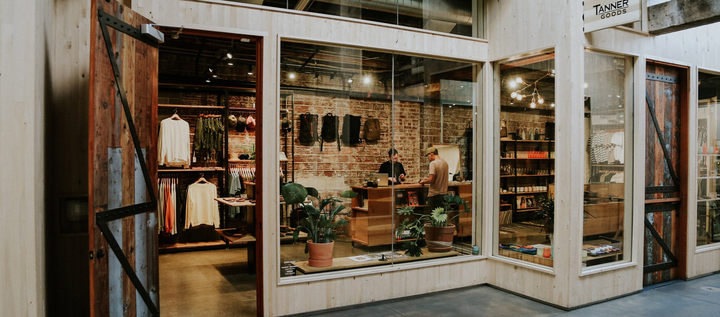 Rustic boutique with wooden doors, brick walls, and curated apparel, bags, and home goods in warm, earthy tones.