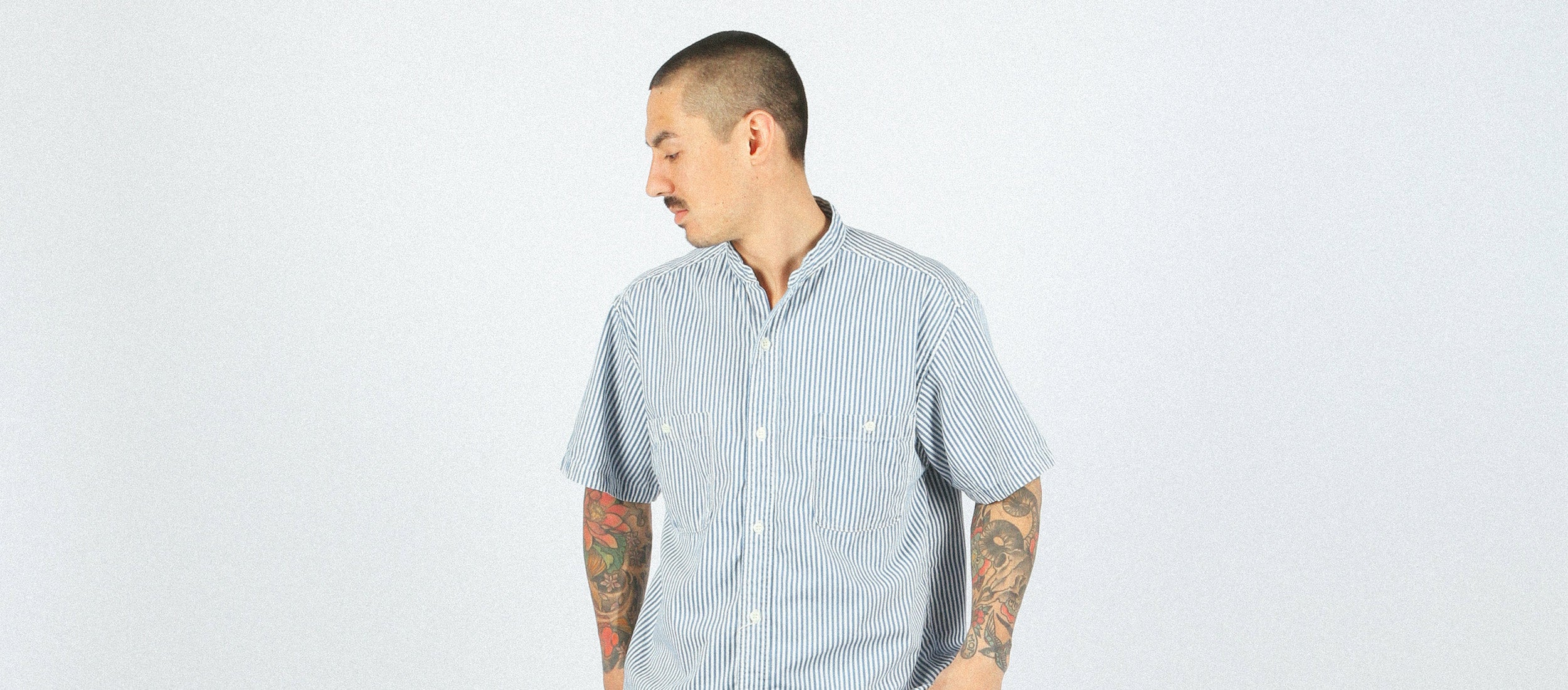 Man in blue and white striped short-sleeve shirt with chest pockets, minimalist style, clean aesthetic.