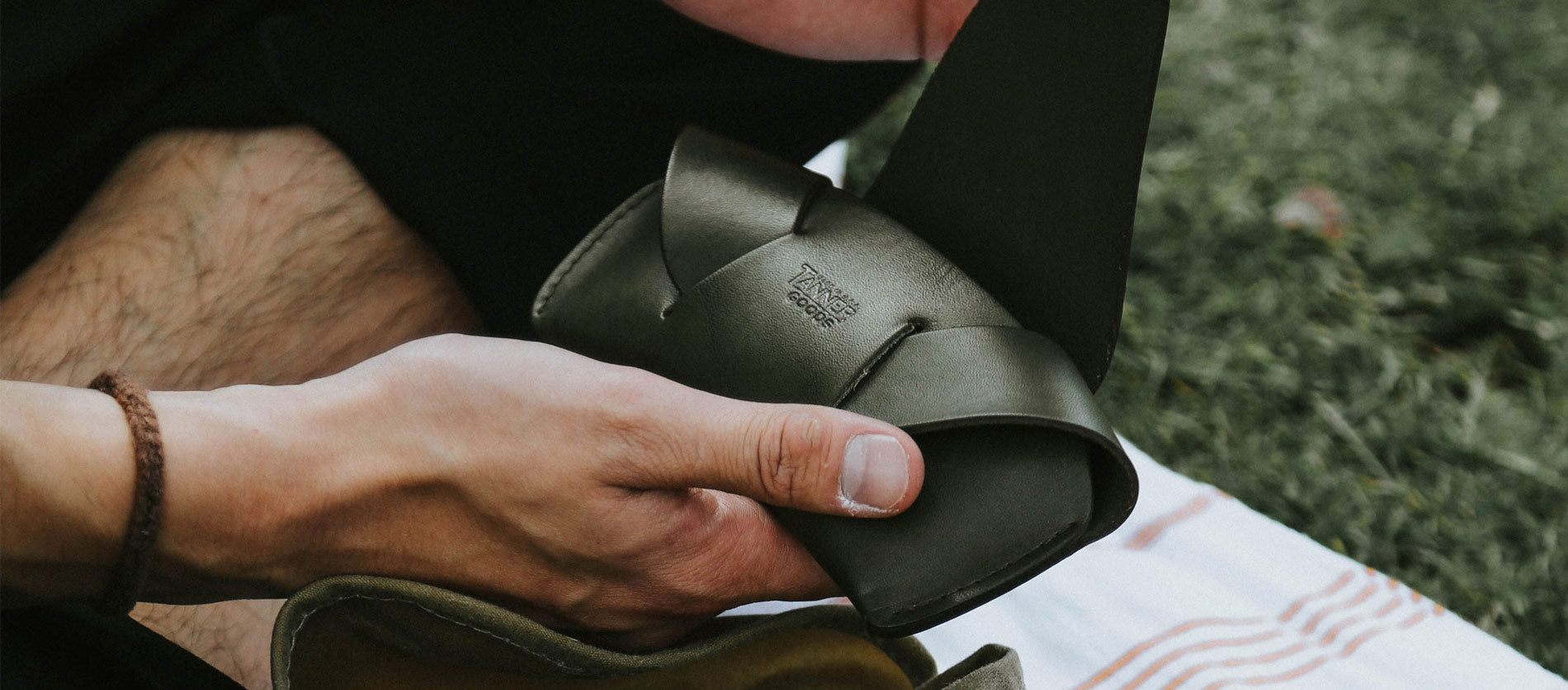 Hand holding olive leather sunglasses case outdoors, rugged style, earthy tones, adventure-ready eyewear.