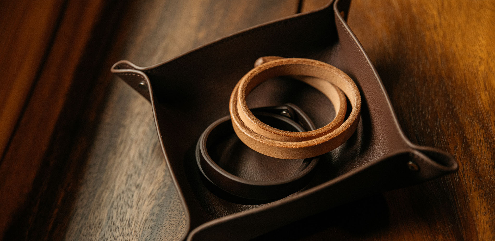 Rich brown leather bracelets and tray on warm wood, showcasing timeless craftsmanship and rustic elegance.