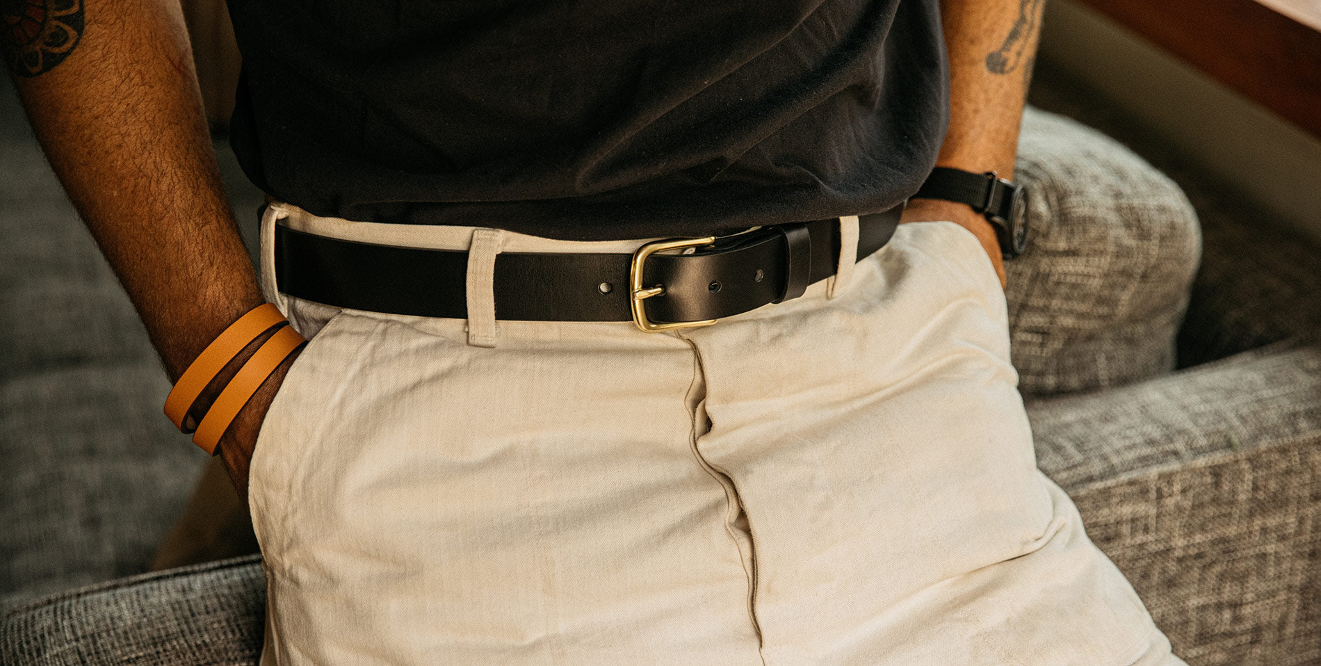 Man wearing black leather belt with gold buckle, paired with khaki pants and orange wristbands, exuding casual sophistication.