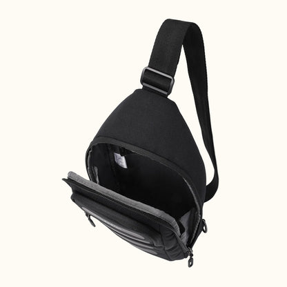 Black fabric sling bag by Hedgren with an open main compartment, adjustable strap, and front stripes.