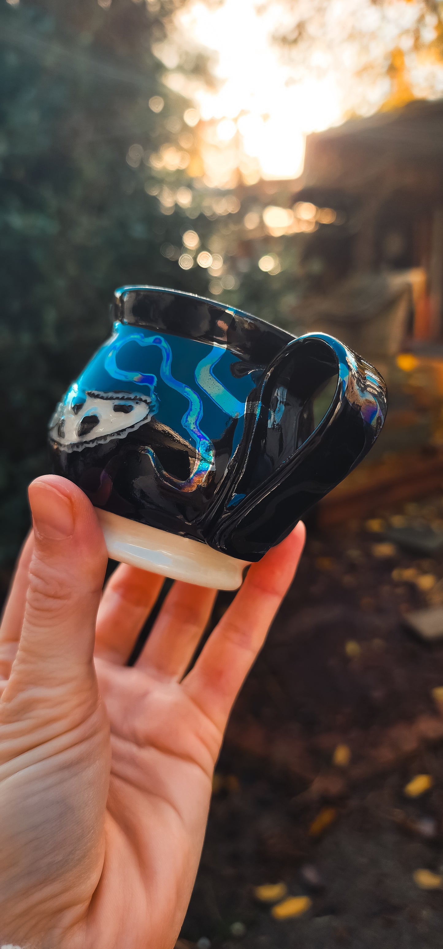 Black ceramic espresso mug with a white slug design and iridescent blue interior, held in a hand.