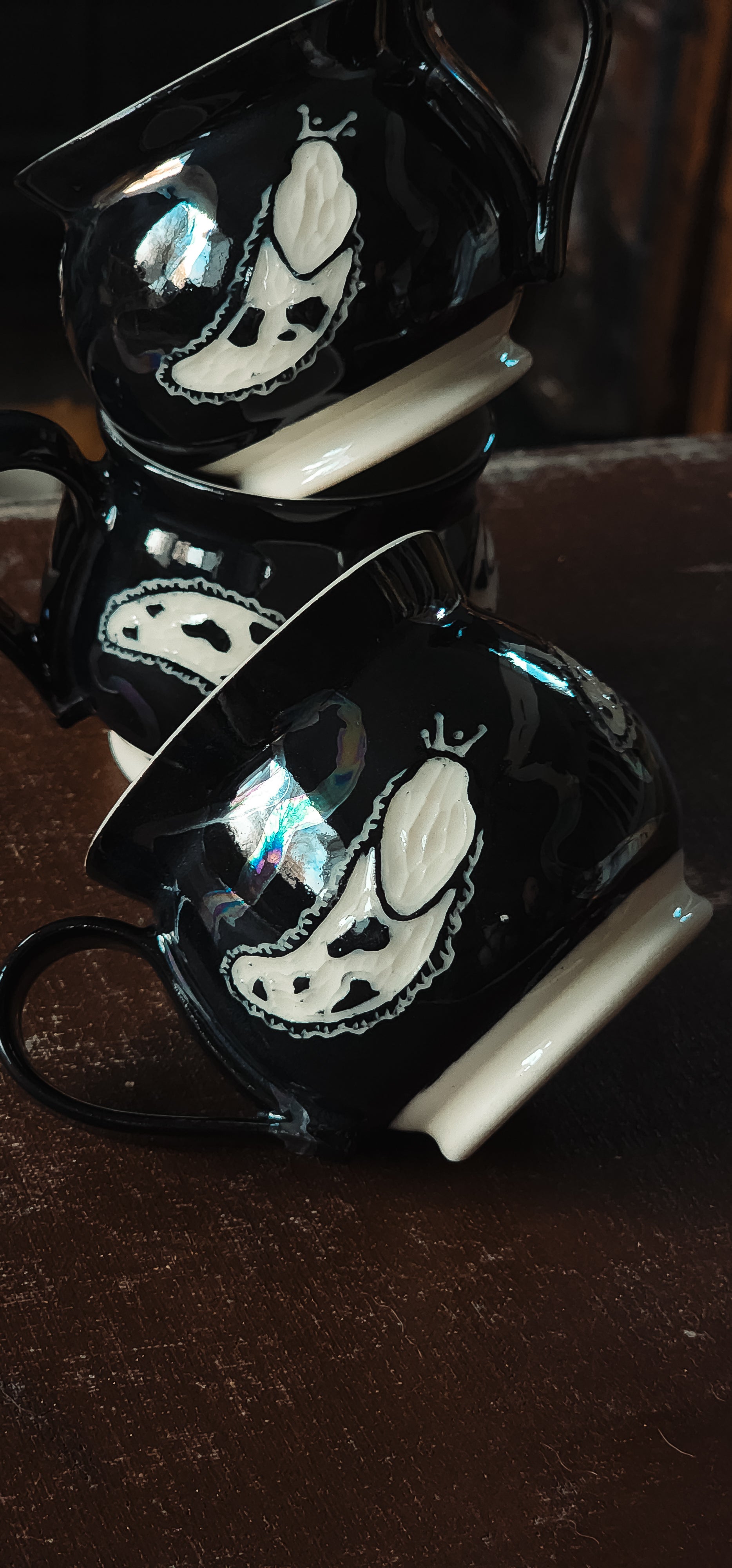 Black ceramic espresso mugs with white slug design, stacked showing iridescent reflections.