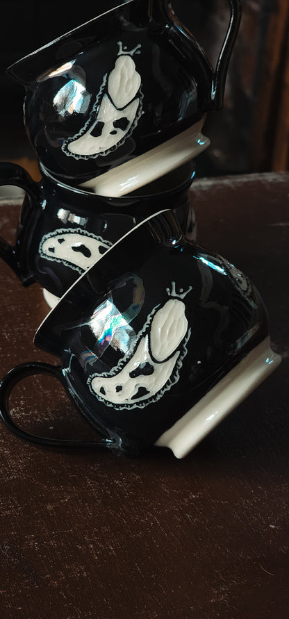 Black ceramic espresso mugs with white slug design, stacked showing iridescent reflections.