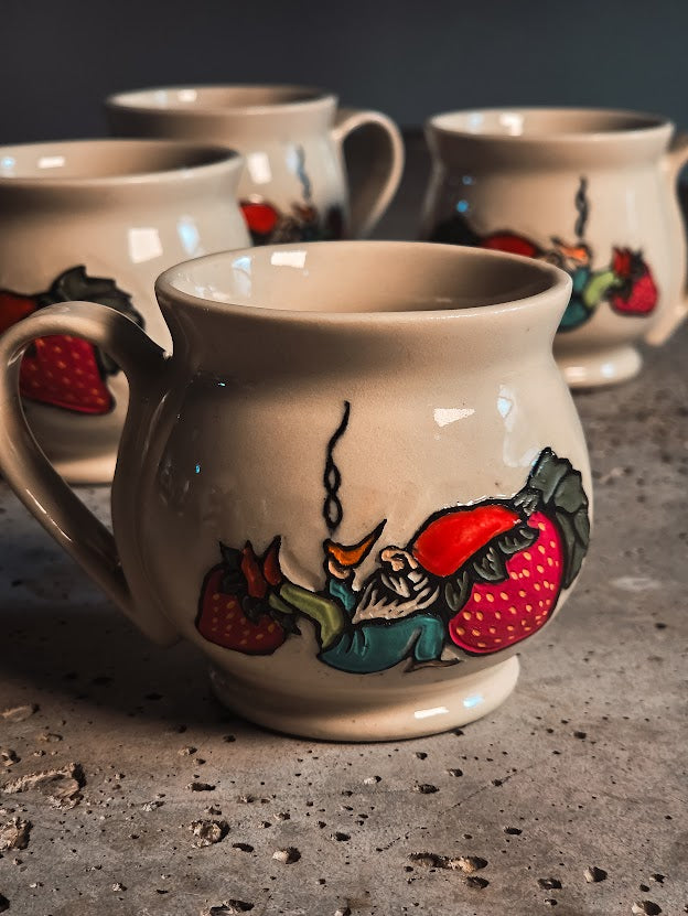 Cream ceramic espresso mug with a hand-painted gnome sitting on strawberries.