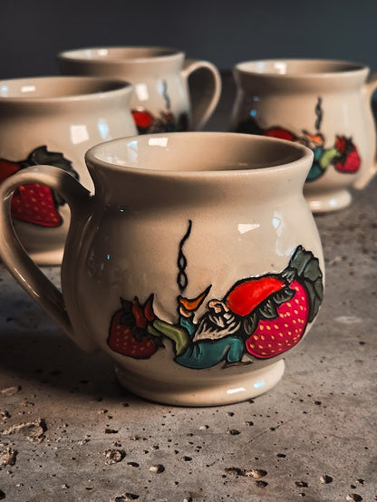 Cream ceramic espresso mug with a hand-painted gnome sitting on strawberries.