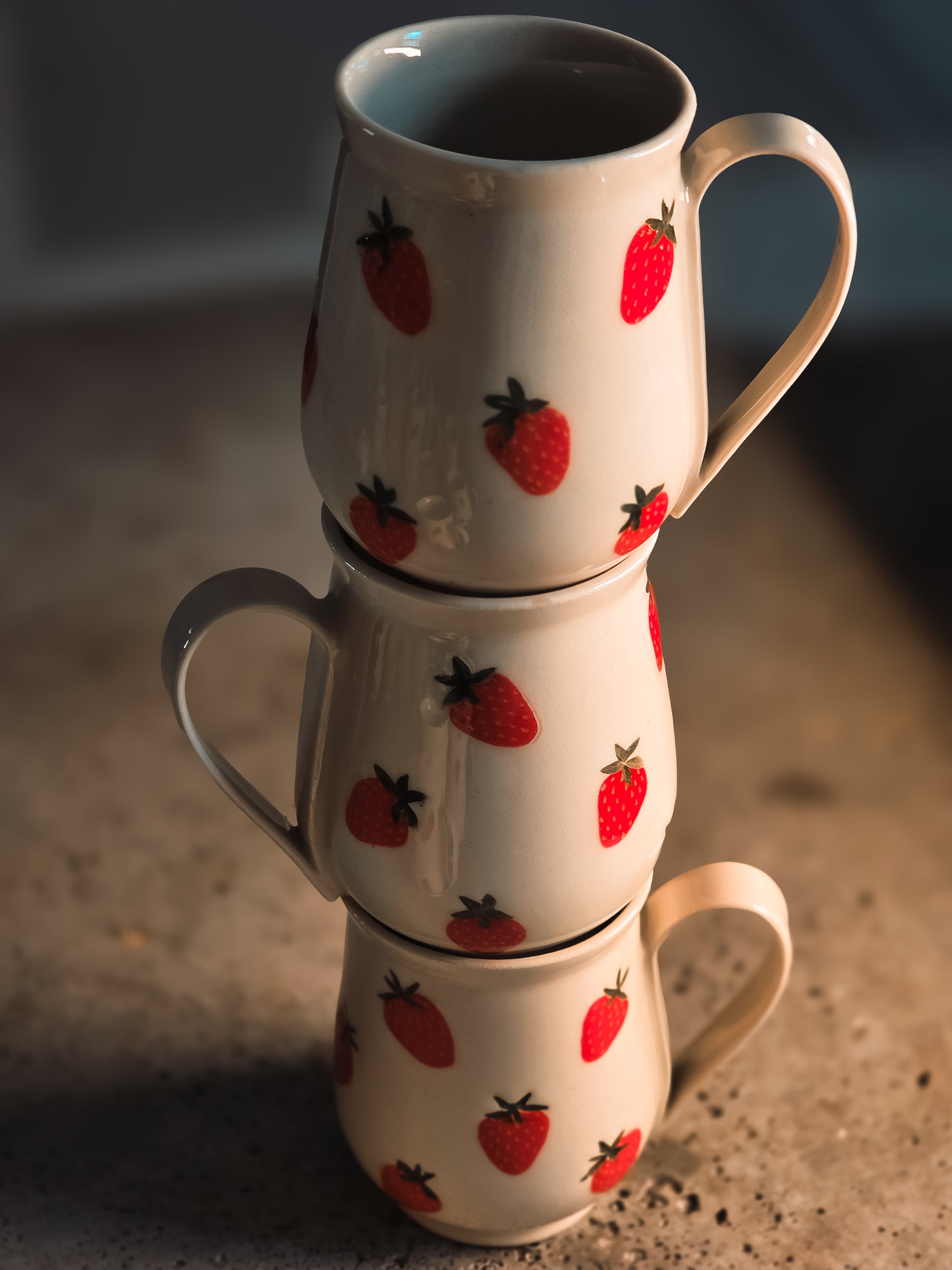 White ceramic strawberry mug with red fruit pattern, stacked three high, glossy finish, side view