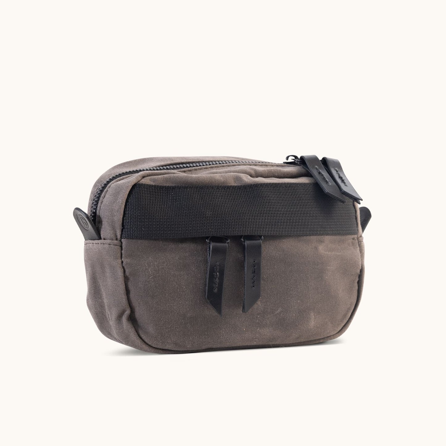 Slate grey waxed canvas crossbody mini bag with a top zipper, two black pull tabs, and a black front strap, angled.
