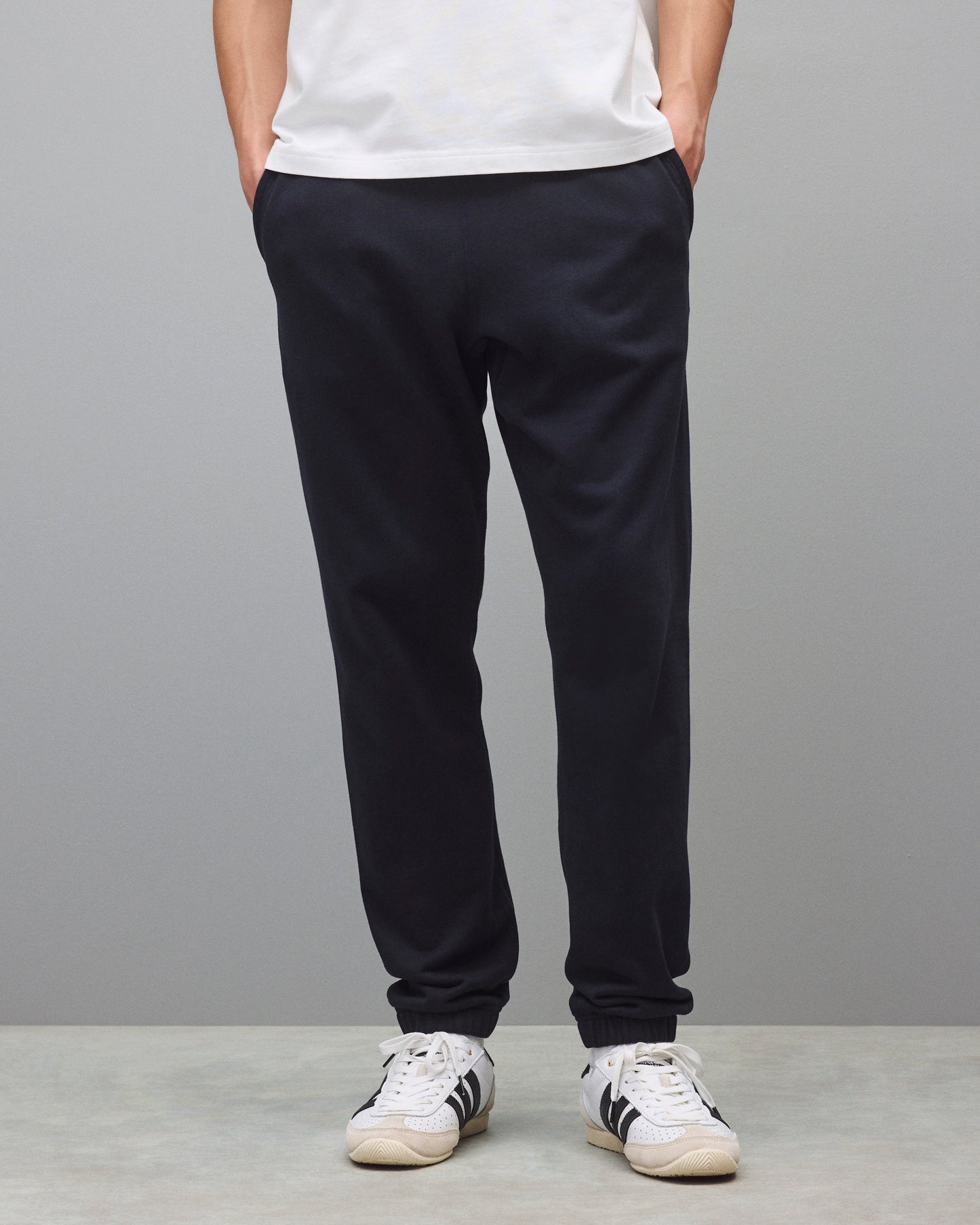Dark navy sweatpants with a relaxed fit and cuffed ankles, styled with a white t-shirt and white sneakers.