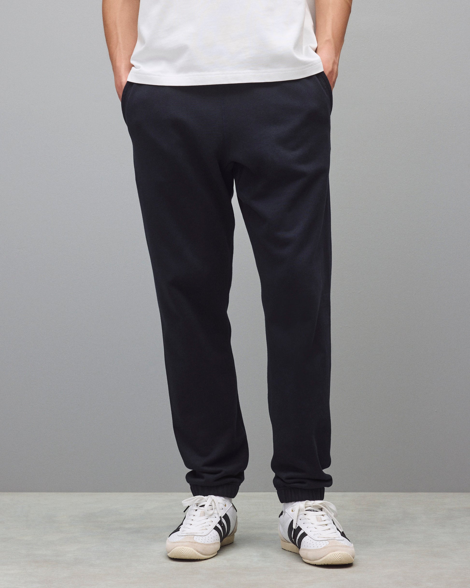 Dark navy sweatpants with a relaxed fit and cuffed ankles, styled with a white t-shirt and white sneakers.