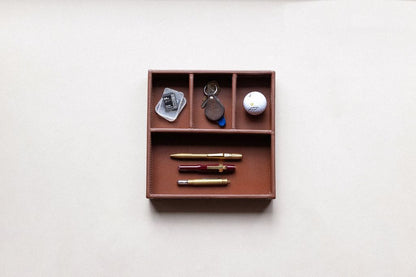 Brown leather supply tray with compartments holding three pens, keys, an SD card, and a golf ball.