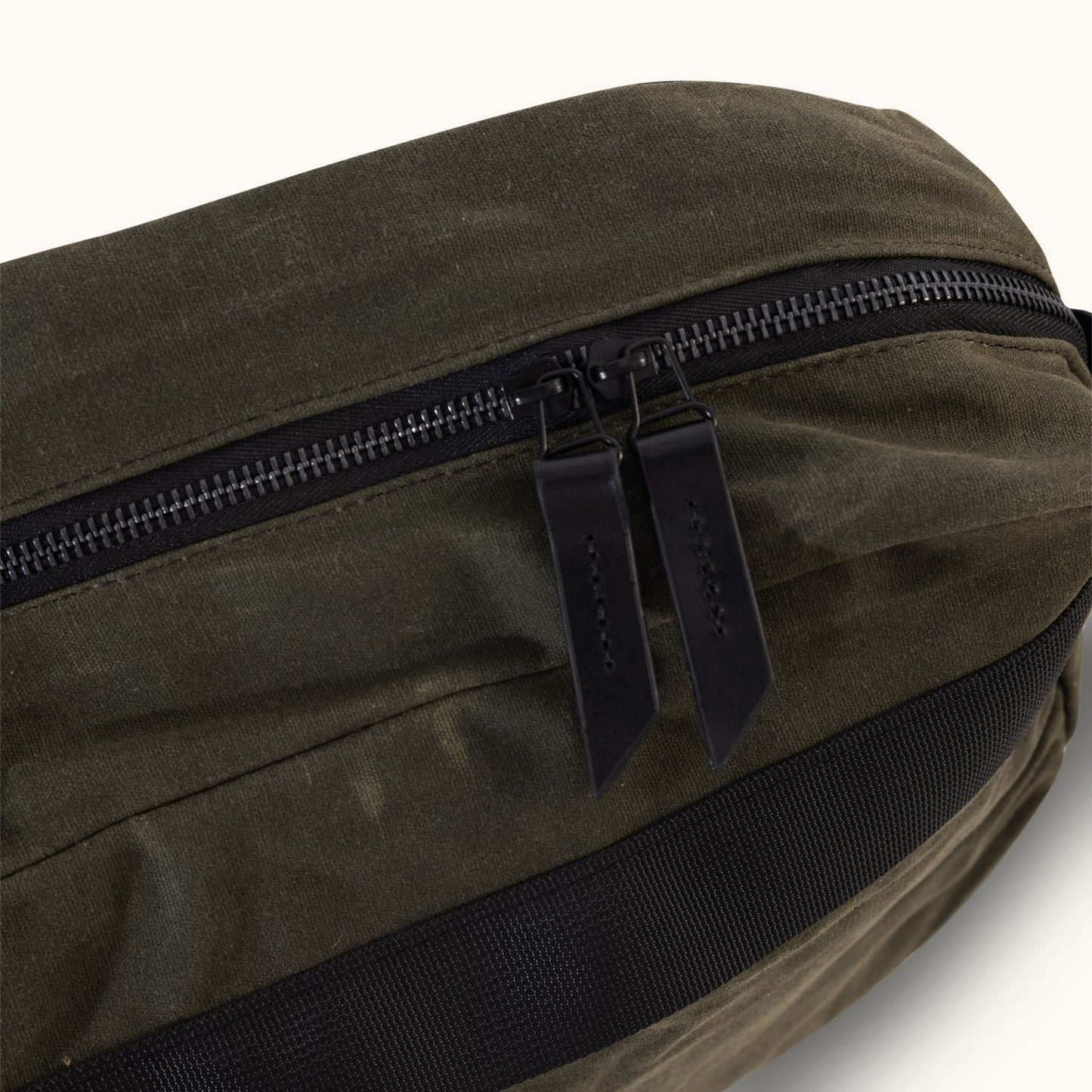 Juniper green waxed canvas crossbody bag with dark zippers, black leather pulls, and black webbing detail.