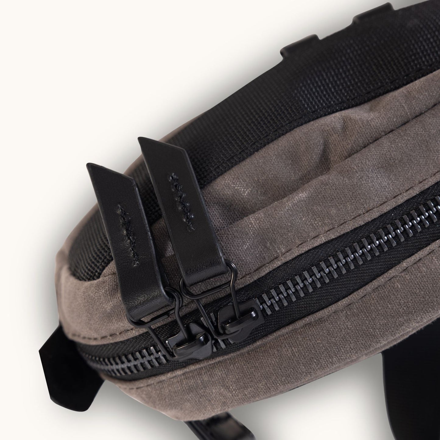 Slate grey waxed canvas crossbody mini bag, close-up top view showing black zipper with two leather pulls and textured black webbing.