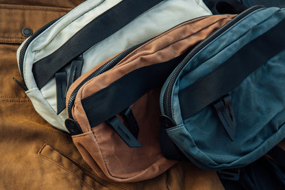 Desert rose waxed canvas Canyon Crossbody Pack, with cream and teal versions featuring black straps and zippers.