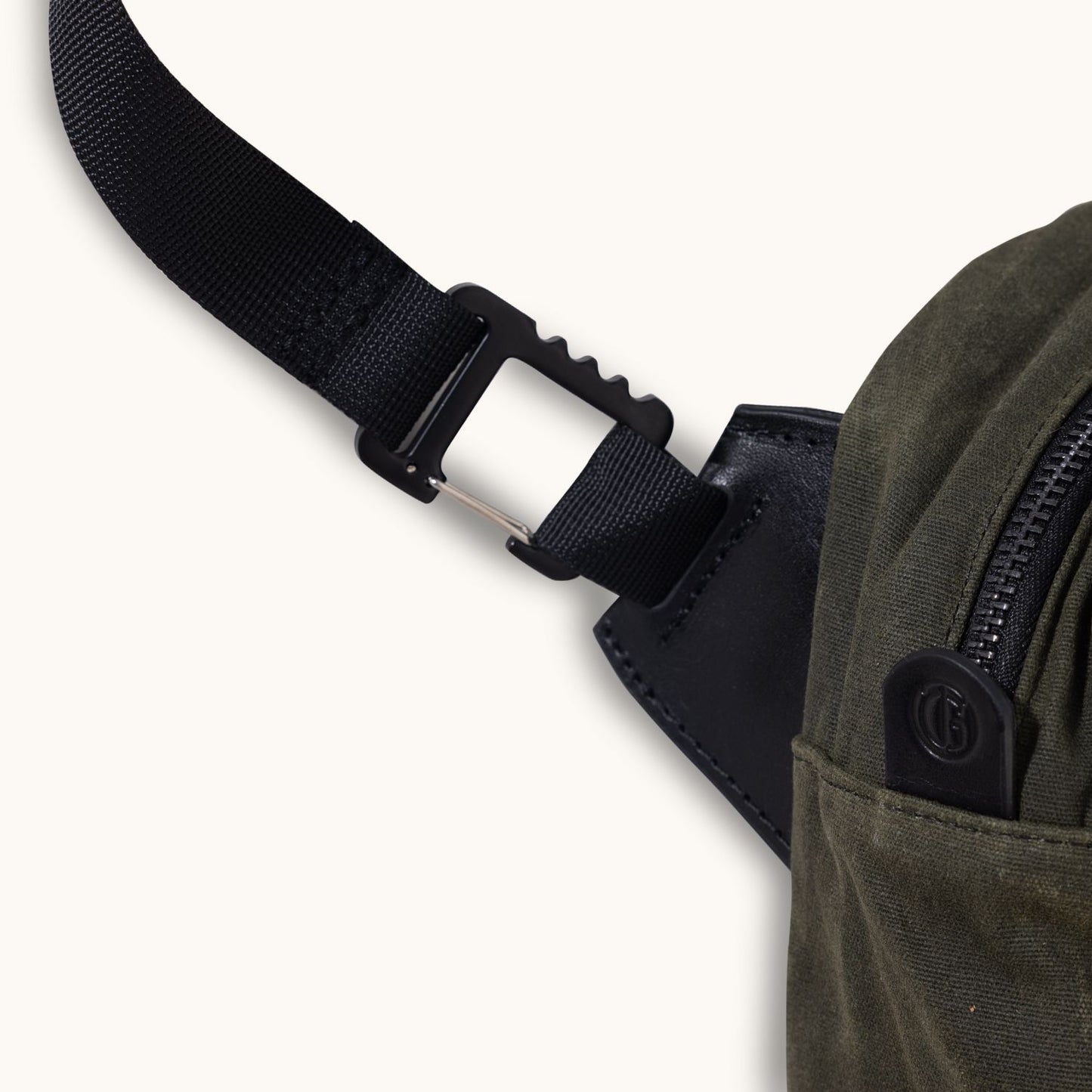 Juniper green waxed canvas Canyon Crossbody bag, with a black webbing strap, black hook clip, zipper, and a small embossed leather logo tab.