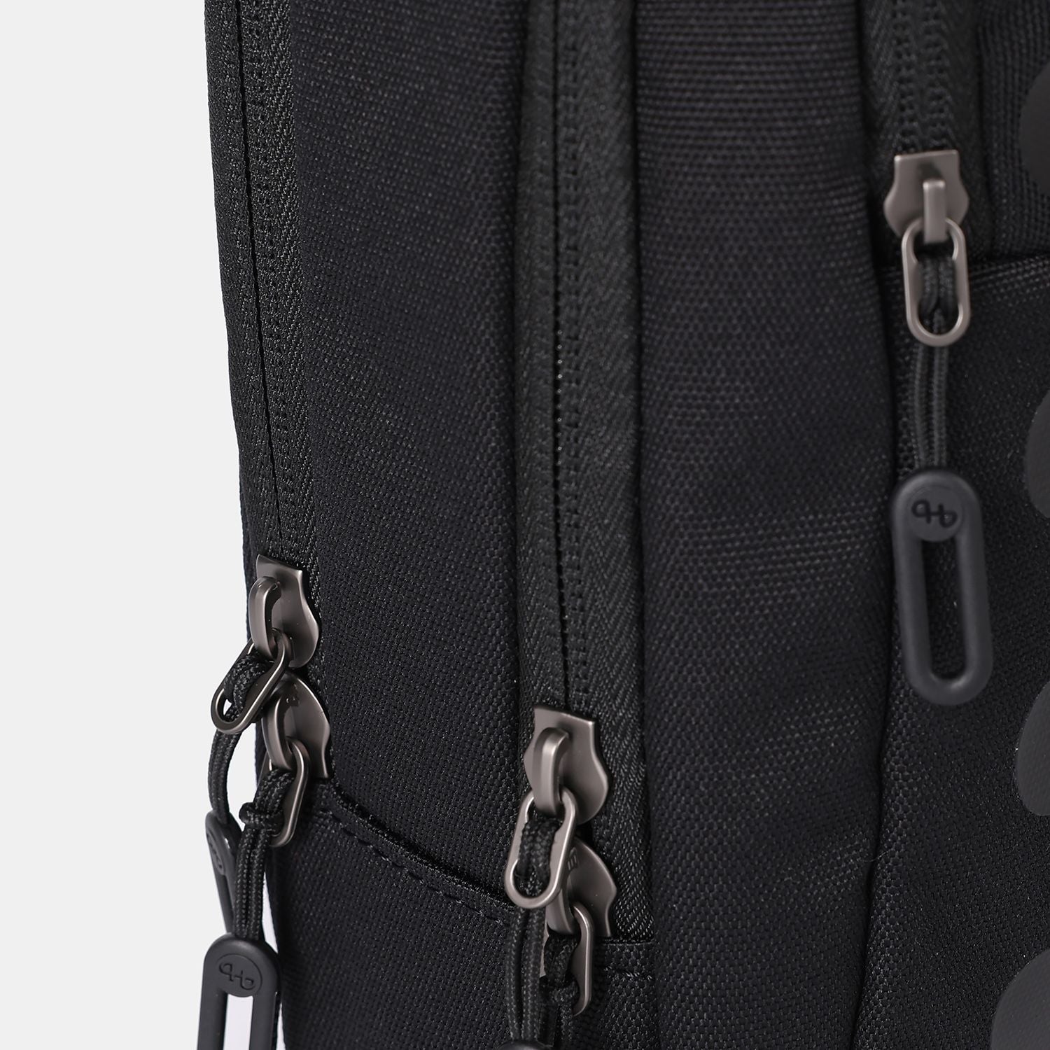 Black sling bag by Hedgren, featuring a textured fabric and multiple dark grey zippers with branded pull tabs.