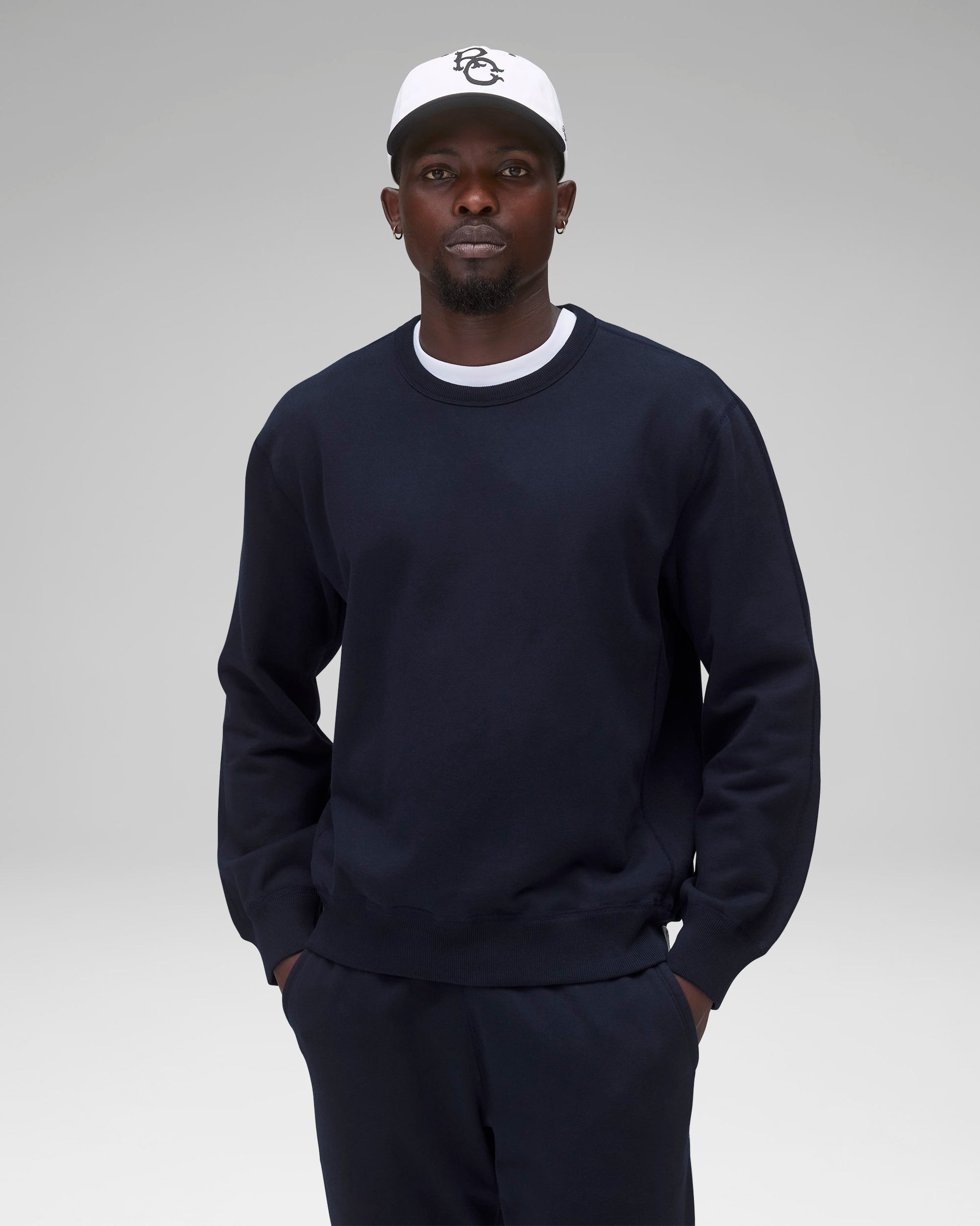 Navy blue midweight terry crewneck worn with matching sweatpants, a white t-shirt, and a white cap.