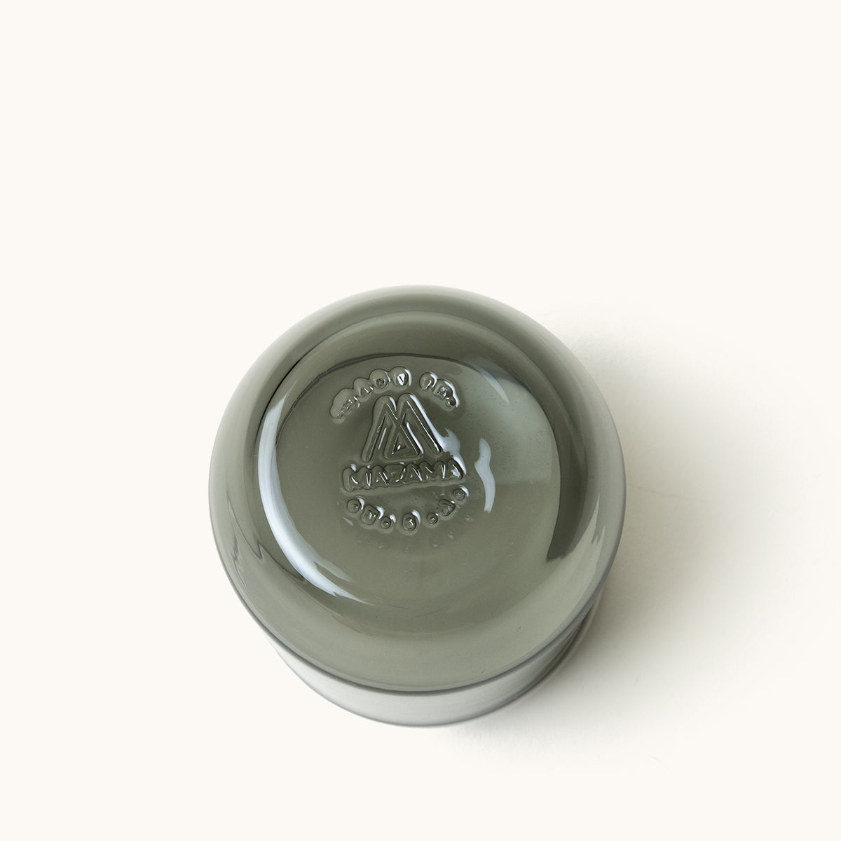 Smoked gray glass cocktail glass with an embossed M-triangle and 'Kiazama' logo on its base, seen from above.