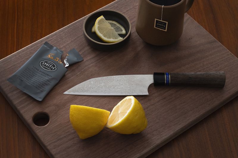 Dark brown walnut cutting board with a circular cutout, displaying a knife, lemon, tea, and mug.